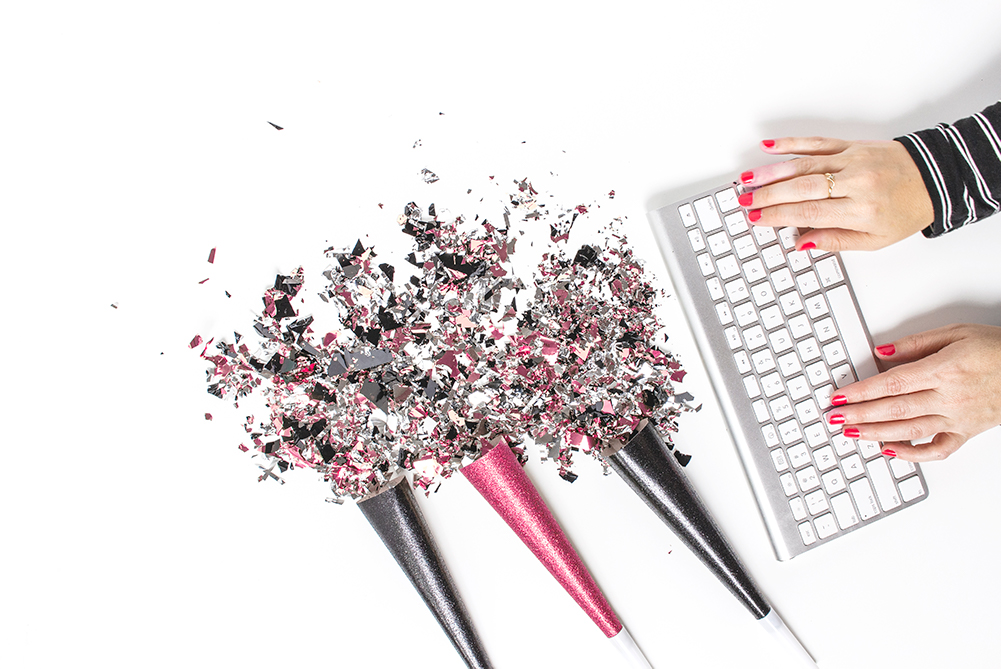 woman's hands with pink nails typing on a keyboard alongside celebration confetti